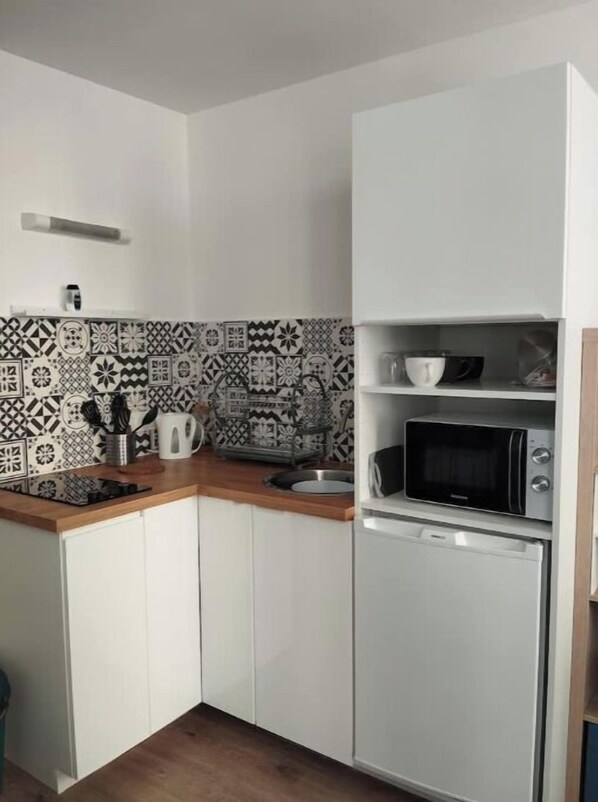Una cocina compacta con armarios blancos, microondas y un salpicadero decorativo.
