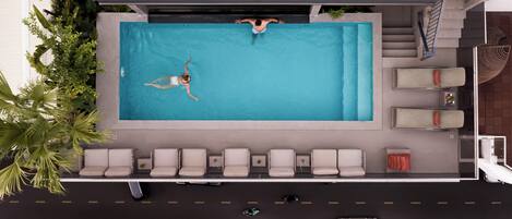 Vue aérienne d’un hôtel avec une piscine, des chaises longues et un parking.