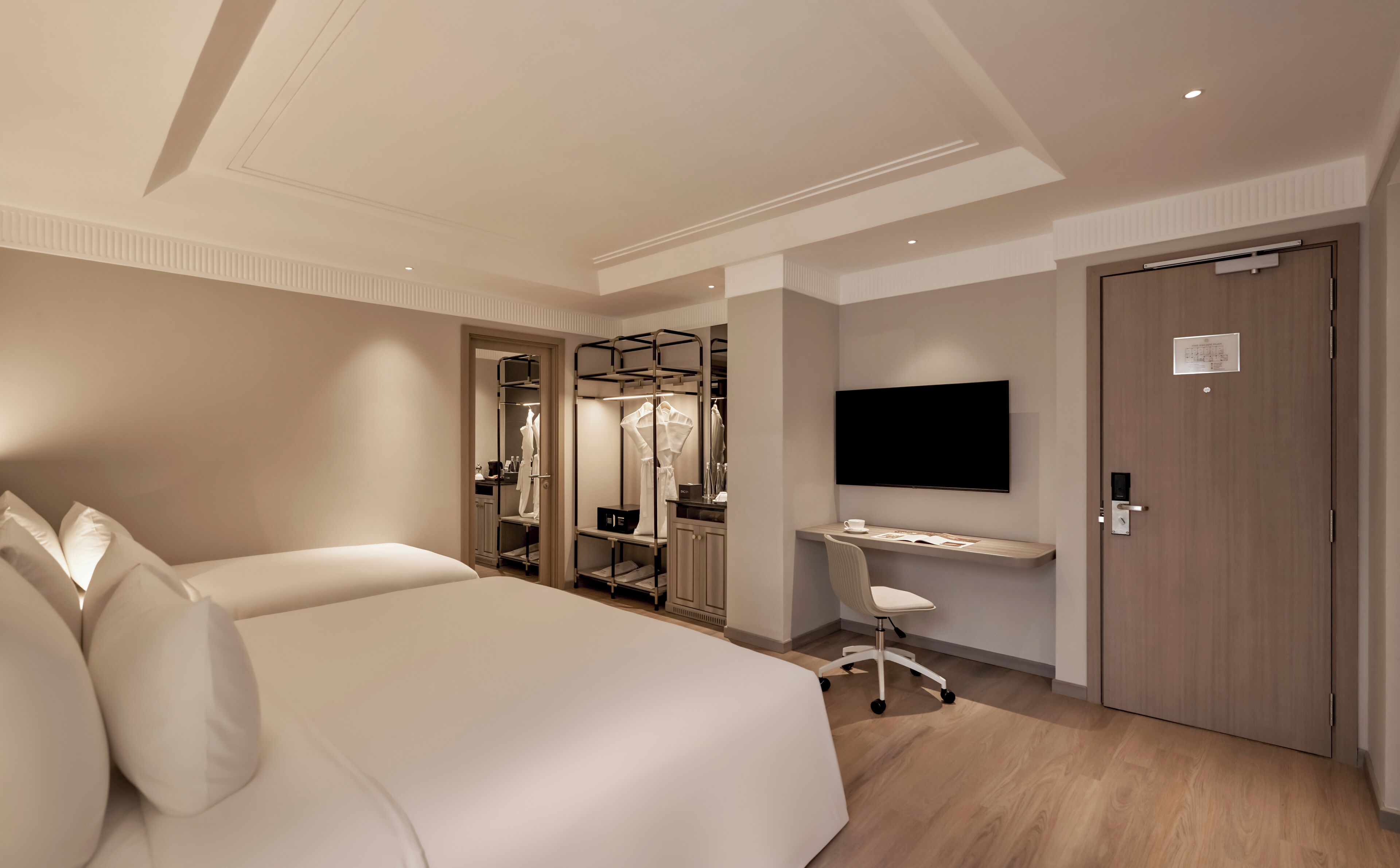 A hotel room with a large bed, a desk, a chair, a TV, and a wardrobe.