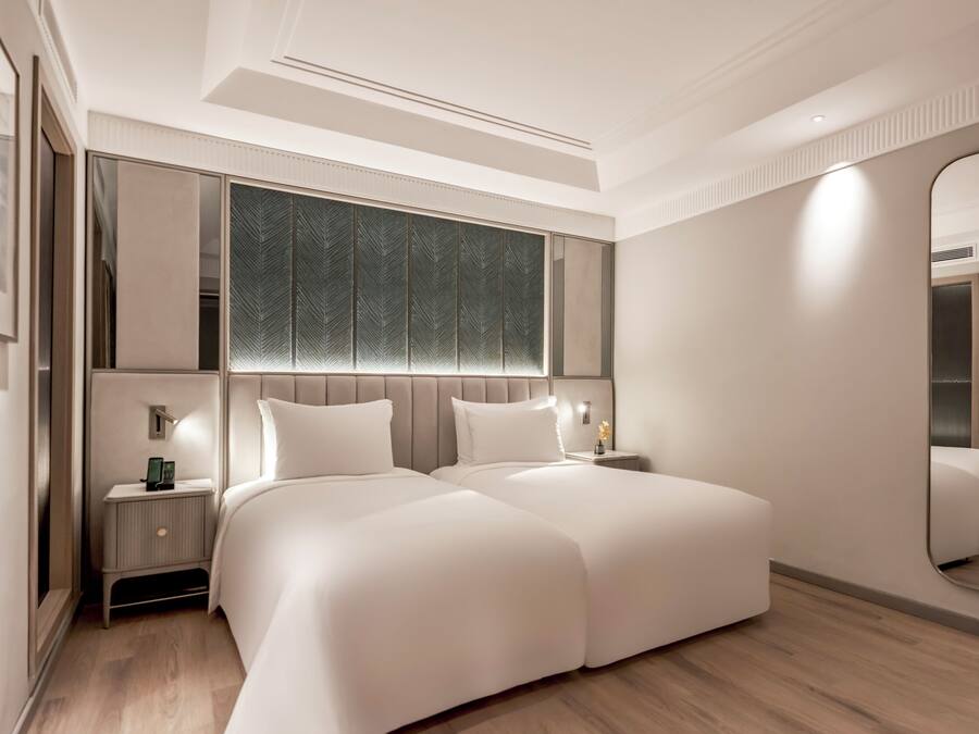 Une chambre à coucher moderne avec un grand lit, des tables de chevet, un miroir et une fenêtre avec un store à motifs de feuilles.