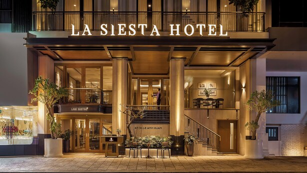 The exterior of La Siesta Hotel with a grand entrance, a staircase leading to the upper floor, and potted plants around the entrance area. - La Siesta Premium Saigon Central (Ho Chi Minh City)