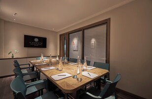 A conference room with a long table, chairs, and a television displaying the hotel name.