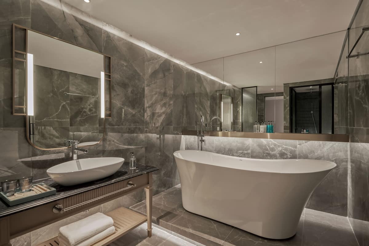 A modern bathroom with a freestanding bathtub, a large mirror, and marble walls.