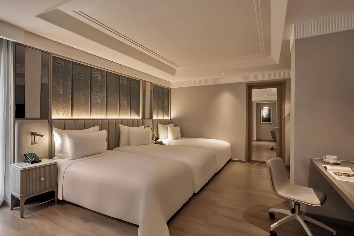 A modern hotel room with two beds, a desk, and a chair.