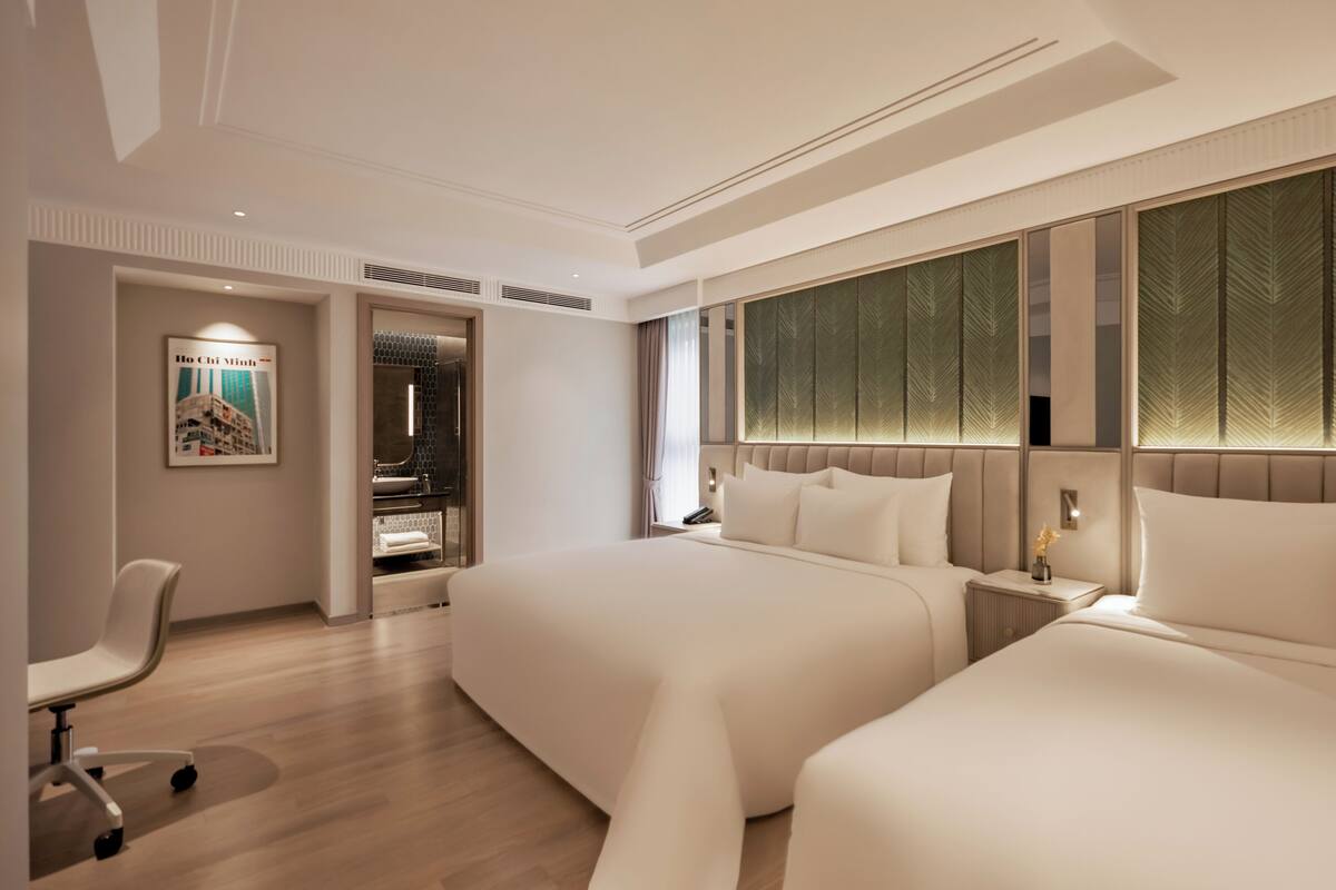 A modern hotel room with two beds, a desk, and a chair.