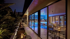 A modern hotel bar with a pool view, featuring a long bar, seating areas, and large windows. - La Siesta Premium Saigon Central (Ho Chi Minh City)