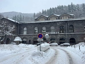 Um edifício com a inscrição 'THERMES' na fachada, rodeado por árvores cobertas de neve e uma paisagem nevada.