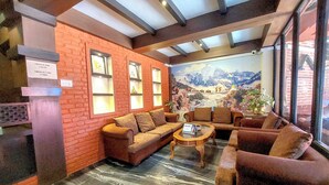 A lobby with a brick wall, a mural of a mountain scene, and seating areas with a coffee table. - Hotel Garuda Bhaktapur (Bhaktapur)