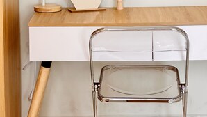 A white desk with a wooden top, a white lamp, a wooden hand sculpture, and a clear glass chair. - LalaHouse Spring Apartment (Ho Chi Minh City)