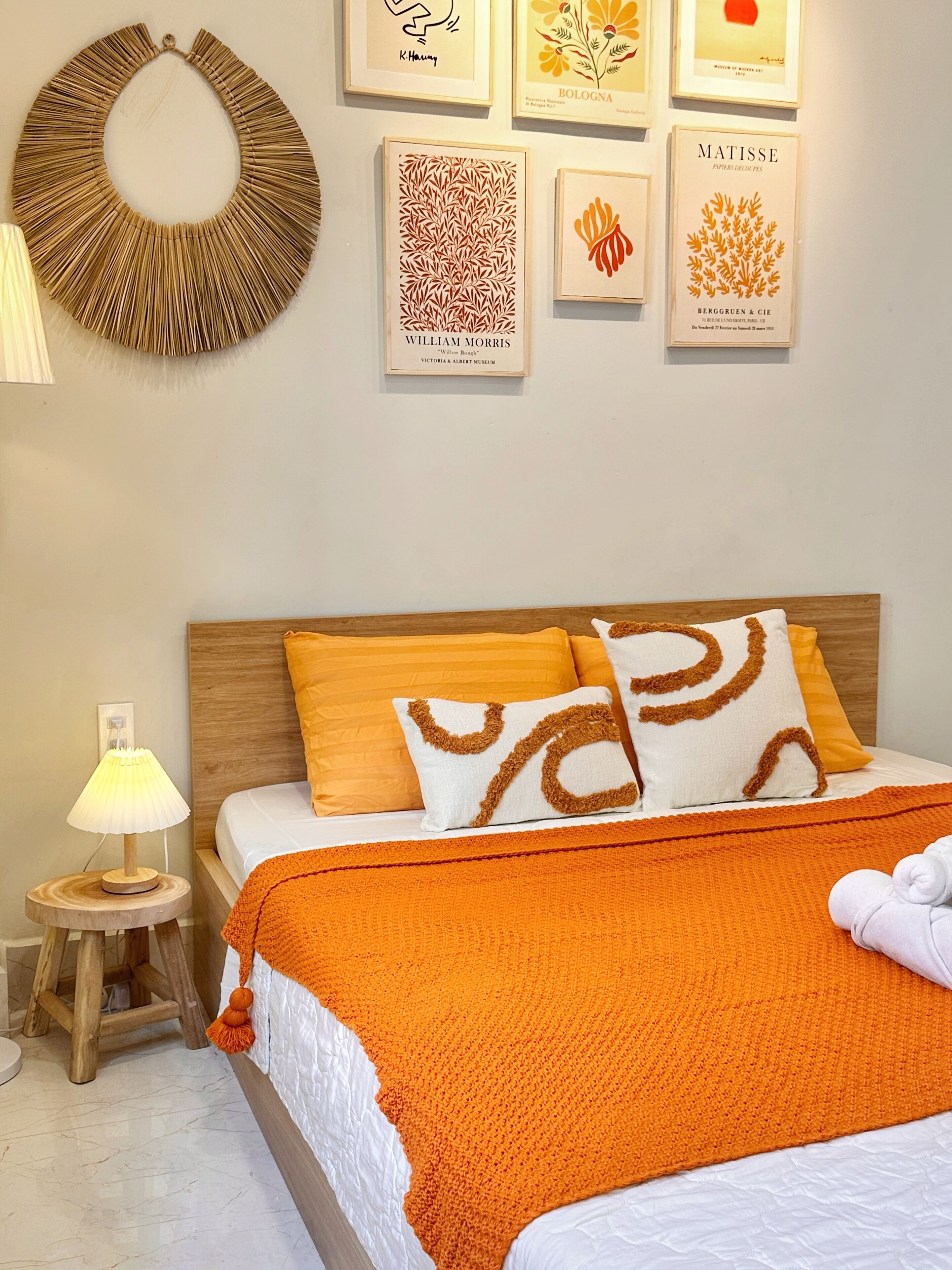 A neatly arranged bedroom with a bed, pillows, a bedside lamp, and framed artworks on the wall.