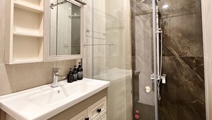 A modern bathroom with a glass-enclosed shower, a white vanity with a mirror, and a marble-tiled floor. - LalaHouse Spring Apartment (Ho Chi Minh City)