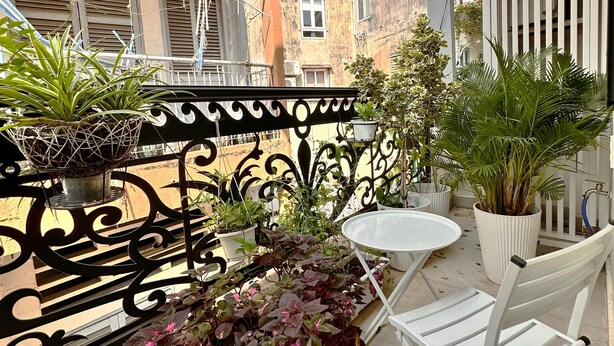 An outdoor balcony with a white table and chairs, surrounded by potted plants and a decorative metal railing. - LalaHouse Spring Apartment (Ho Chi Minh City)