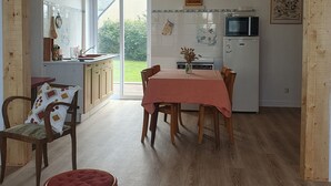 A spacious kitchen with wooden cabinets, a dining table with chairs, and a view through a glass door to a garden. - The old Caon grocery store (Telgruc-sur-Mer)