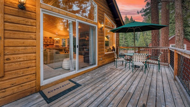 A wooden cabin with a deck, large windows, and a green umbrella.