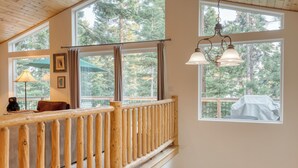 A wooden balcony with a railing, large windows with curtains, and a hanging light fixture.