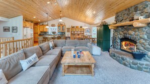 A cozy living room with a stone fireplace, wooden ceiling, and a sofa with a pillow labeled "LAKE TAHOE."