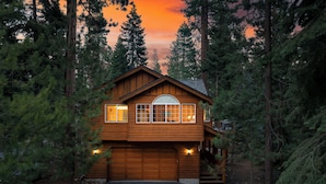 A two-story log cabin with a large garage, surrounded by tall pine trees.