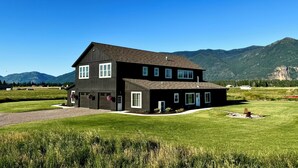Une maison noire à deux étages avec un garage, entourée d’une pelouse bien entretenue et avec des montagnes en arrière-plan.