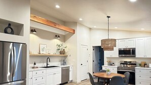 Une cuisine moderne dotée d’appareils électroménagers en acier inoxydable, de meubles blancs et d’une table à manger en bois avec des chaises.