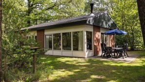 A small, single-story building with large windows, a brick exterior, and a patio area with outdoor seating. - Detached bungalow for 6 persons (Putten)