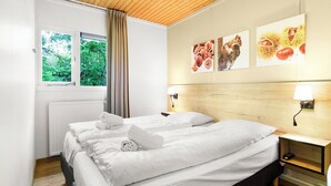 A hotel room with a large bed, two bedside tables, a window with curtains, and wall art depicting fruits and nuts. - Detached bungalow for 6 persons (Putten)