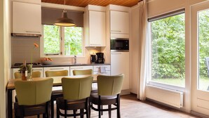 A modern kitchen with white cabinets, a dining table with chairs, a hanging light fixture, and a view of greenery through large windows. - Detached bungalow for 6 persons (Putten)