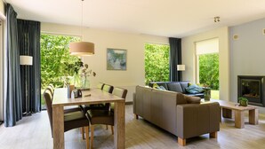 A modern living room with a dining area, large windows, and a fireplace. - Detached 6-person villa (Ruinen)