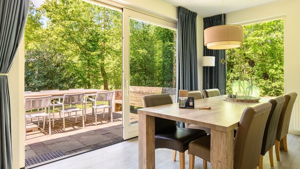 A dining area with a wooden table, chairs, and a pendant light. - Detached 6-person villa (Ruinen)