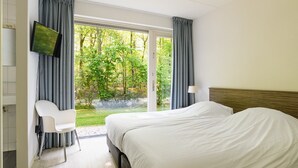 A hotel room with two beds, a TV, and a view of a garden. - Detached 6-person villa (Ruinen)