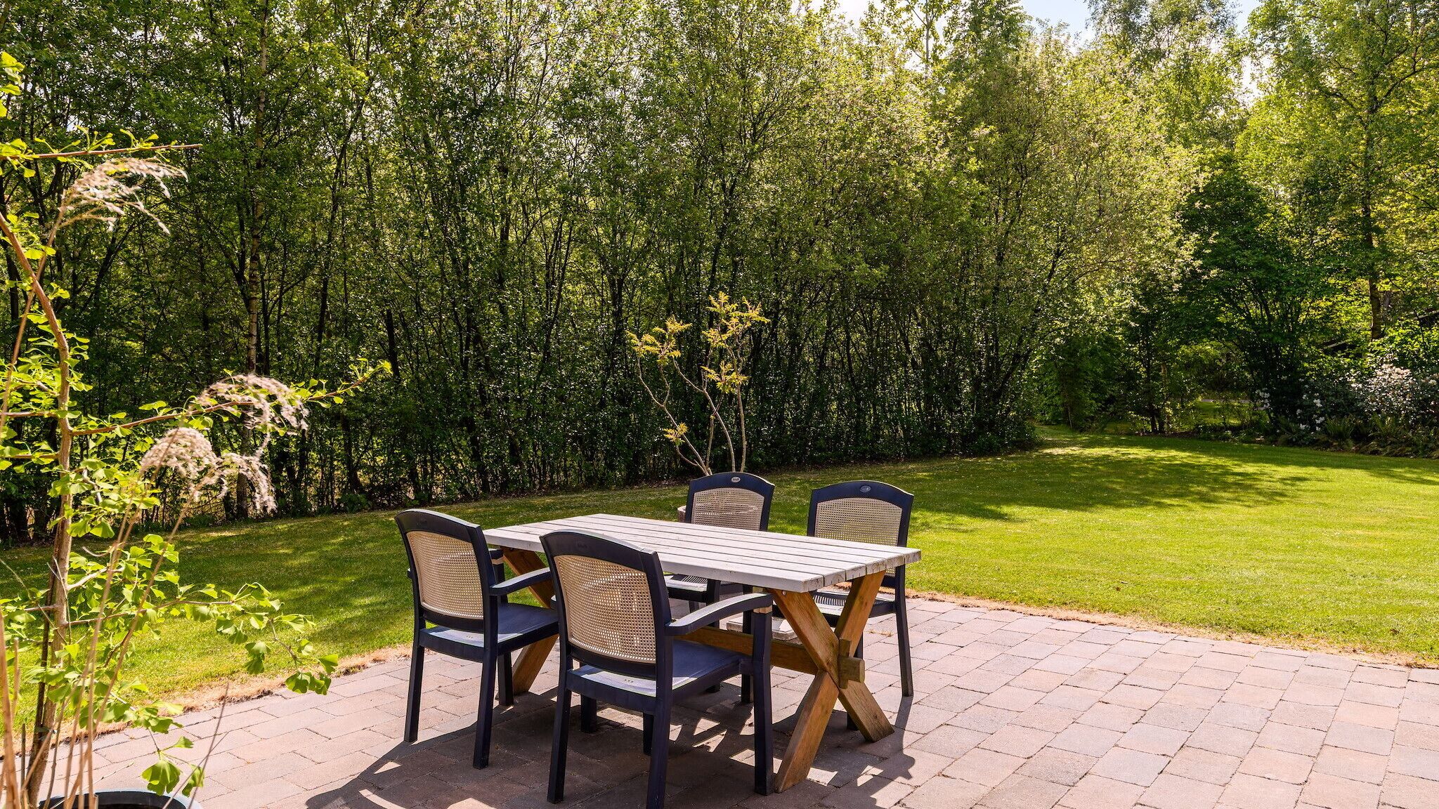 En udendørs terrasse med et bord og stole, omgivet af en frodig grøn hæk.