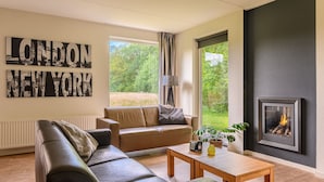 Una sala de estar moderna con un sofá de cuero, una mesa de centro y una chimenea. Hay dos ventanas amplias con cortinas, y una obra de arte con una vista urbana en la pared.