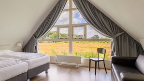 Un dormitorio con dos camas, un radiador, una silla y vistas a un campo a través de amplios ventanales.