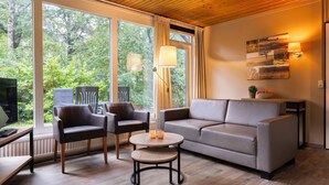 A modern living room with a sofa, two armchairs, a coffee table, and a floor lamp. Large windows offer a view of a lush garden.