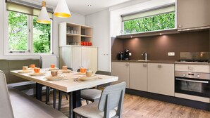 A modern kitchen with a dining area, featuring a built-in oven, a coffee maker, and a view of greenery through the windows. - Comfortable 8-person bungalow (Putten)