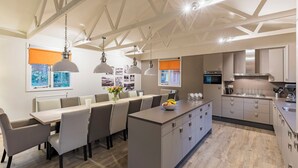 Una cocina moderna con una isla central, iluminación colgante y una zona de comedor con una mesa larga y sillas.