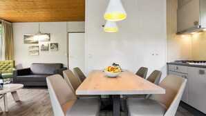 A modern dining area with a wooden table, grey upholstered chairs, and a bowl of fruit.
