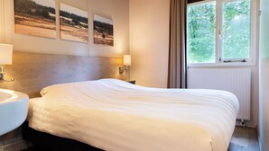 A hotel room with a bed, a nightstand, a lamp, a window, and three framed pictures on the wall. - Comfortable bungalow for 4 persons (Putten)