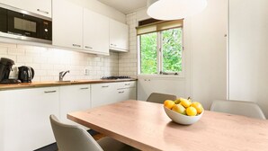 A modern kitchen with white cabinets, a built-in microwave, a coffee maker, and a bowl of fruit on the table. - Comfortable bungalow for 4 persons (Putten)