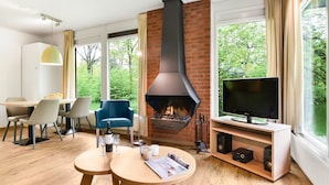 A modern living room with a fireplace, a dining area, and a TV. - Comfortable bungalow for 4 persons (Putten)