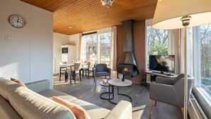 A modern living room with a fireplace, a dining area, and a TV. - Semi-detached bungalow for 4 persons (Putten)