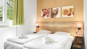 A hotel room with two beds, a wooden headboard, wall-mounted lamps, and three framed pictures depicting nature scenes. - Semi-detached bungalow for 4 persons (Putten)