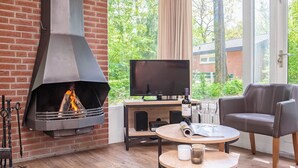 A modern living room with a fireplace, a flat-screen TV, a leather sofa, and a round wooden table. - Semi-detached bungalow for 4 persons (Putten)