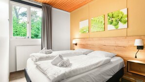 Hotellihuone, jossa on suuri sänky, ikkuna verhoilla, patteri ja kolme seinälle ripustettua taulua, joissa on kuvattuna lehtiä.