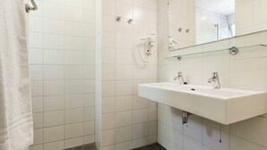 Kylpyhuone, jossa on valkoiset laatat, lasihylly, pesuallas ja suihku.
