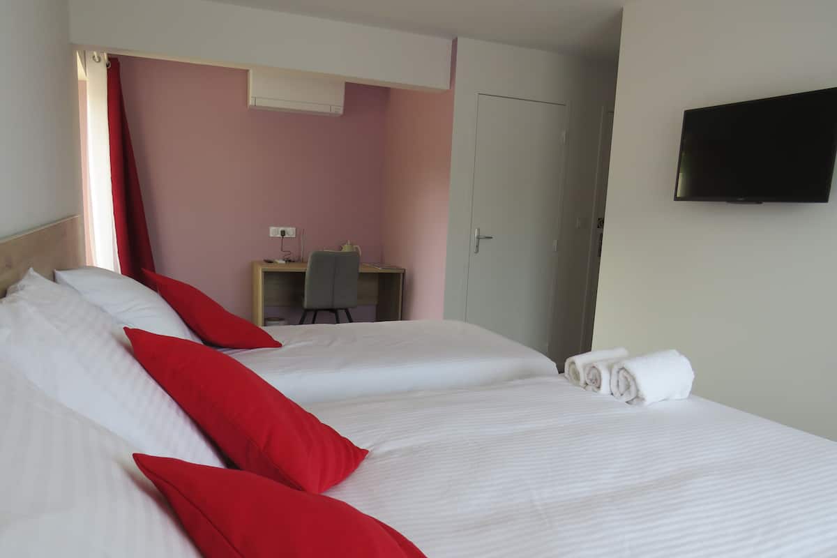 A hotel room with two beds, a desk, a chair, a TV, and a wardrobe.