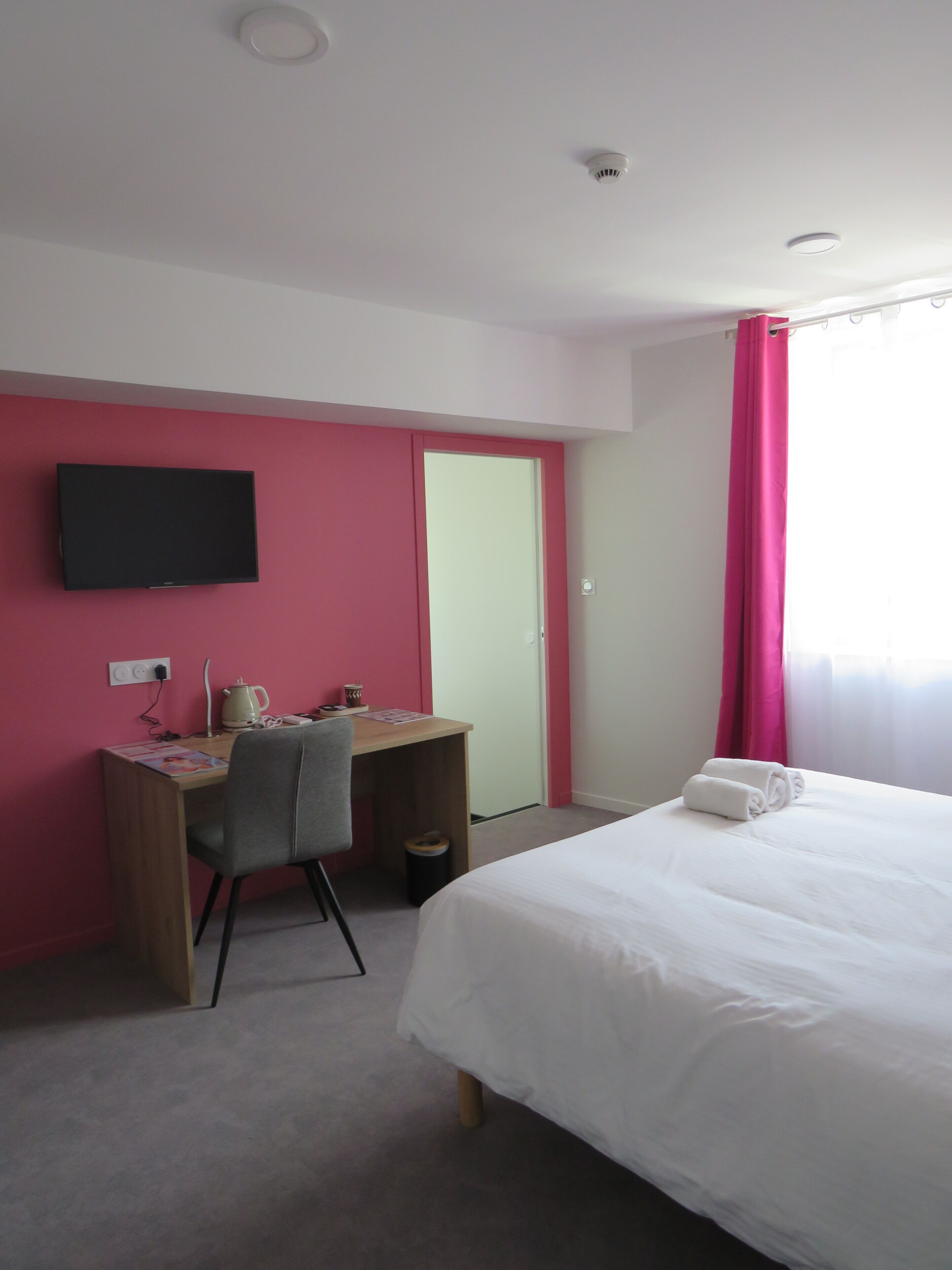 A hotel room with a bed, a desk, a chair, a television, and a window with curtains.