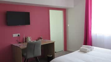 A hotel room with a bed, a desk, a chair, a television, and a window with curtains.