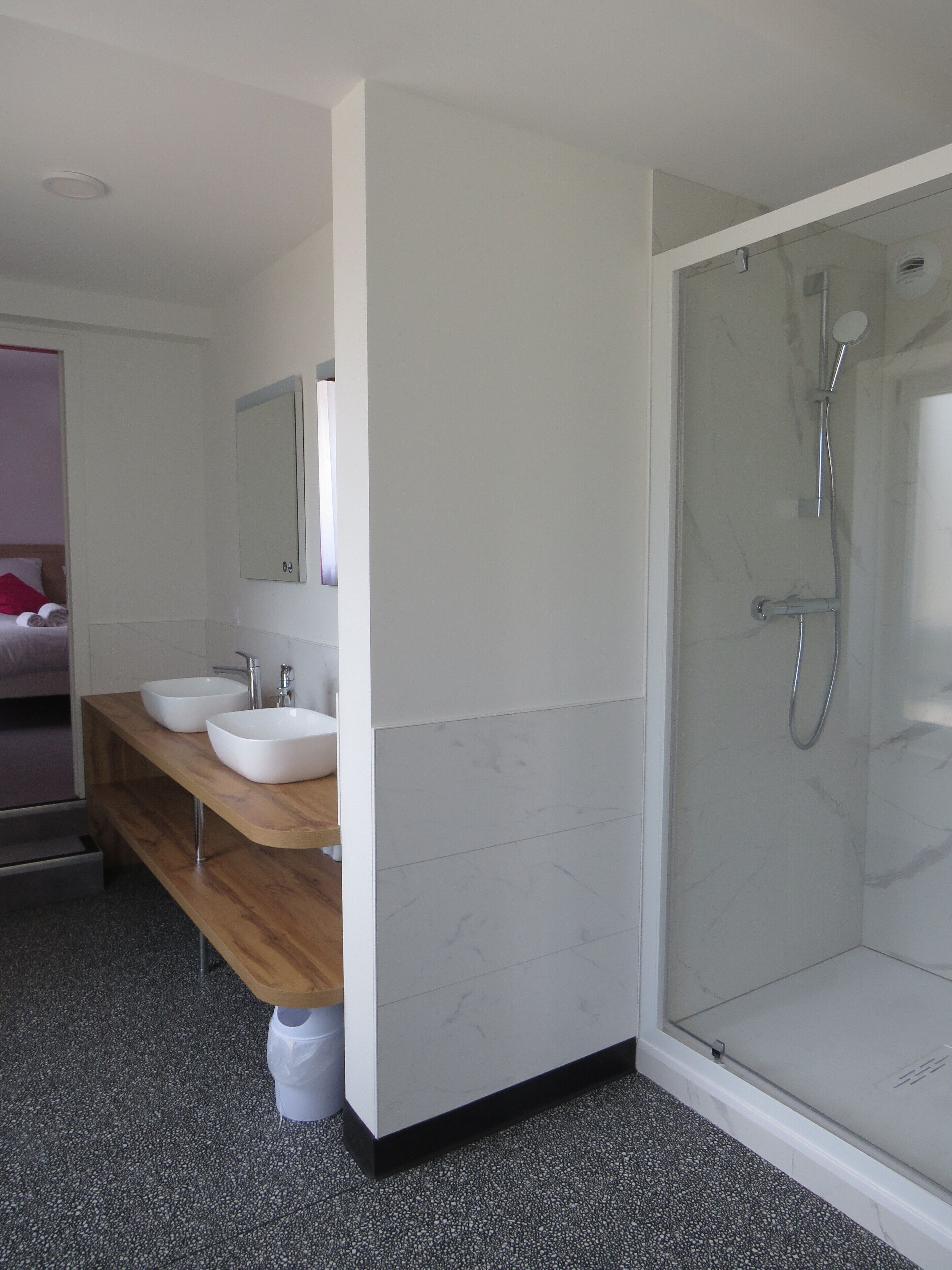 A modern bathroom with two sinks, a shower, and a wooden vanity.