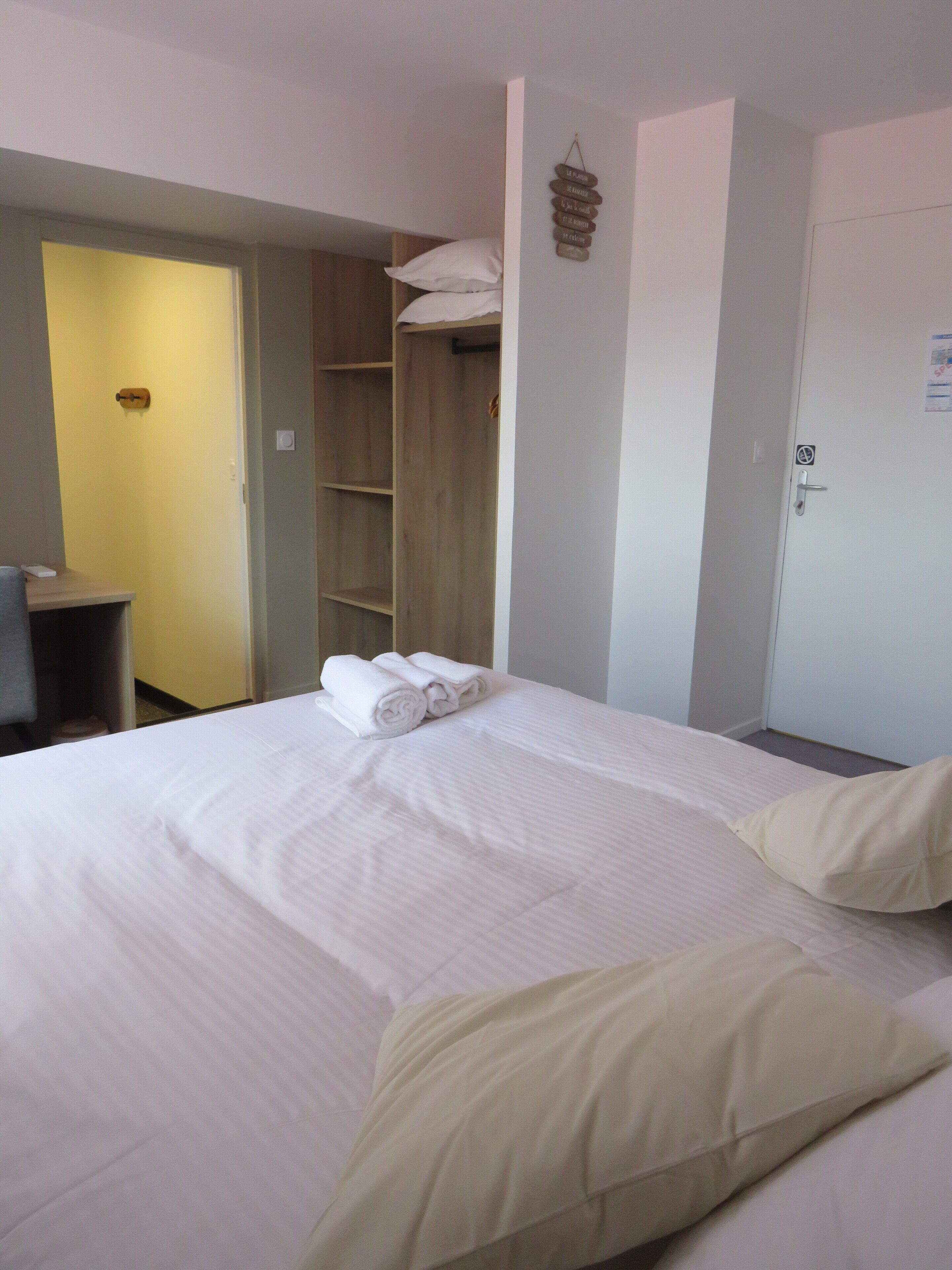Una habitación de hotel con una cama, un armario, un escritorio y una puerta.