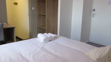 A hotel room with a bed, a wardrobe, a desk, and a door.